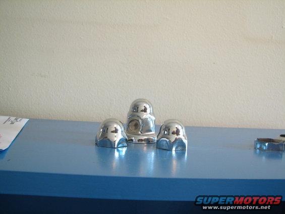 Three chrome lug nut covers on a blue surface