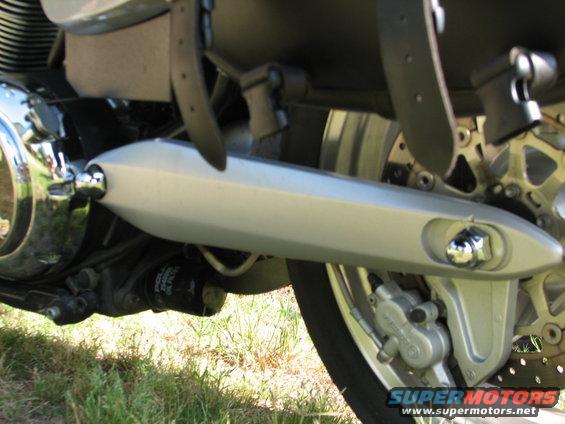 Close-up of motorcycle exhaust pipe, rear wheel, and brake caliper. Oil filter visible underneath