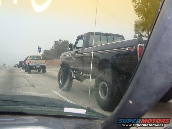 Several lifted pickup trucks driving in a line on a foggy highway