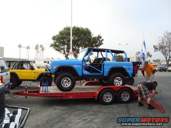 Blue Ford Bronco with roll cage on a trailer, yellow Ford Bronco behind it