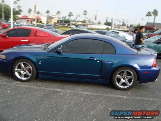Blue coupe parked in a lot, red car next to it. People in background