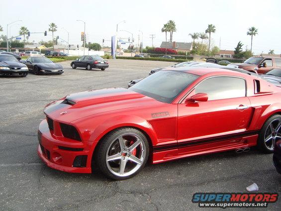 Red Ford Mustang with a hood scoop and black racing stripes, parked on asphalt