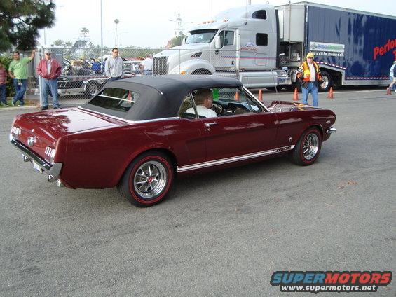 Maroon convertible classic car with a black top, side stripe, and red-line tires, viewed from the rear three-quarter angle