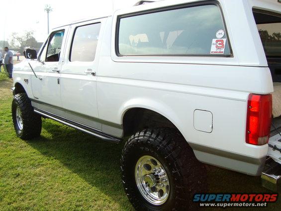 White SUV with lifted suspension and large tires, parked on grass. Has a sticker on the rear window