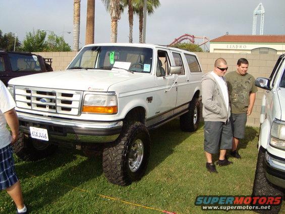 White SUV with lifted suspension and large tires, front quarter view. Two men stand nearby