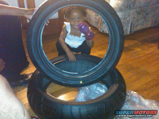 Two tires stacked, with a child holding a purple bottle visible through the top tire
