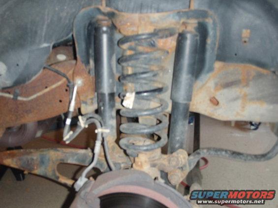 Close-up of rusty suspension parts, including shocks and coil springs, with a brake rotor visible