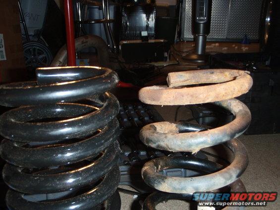 Two coil springs, one black and new-looking, the other rusty and old. They are sitting on a keyboard in a garage