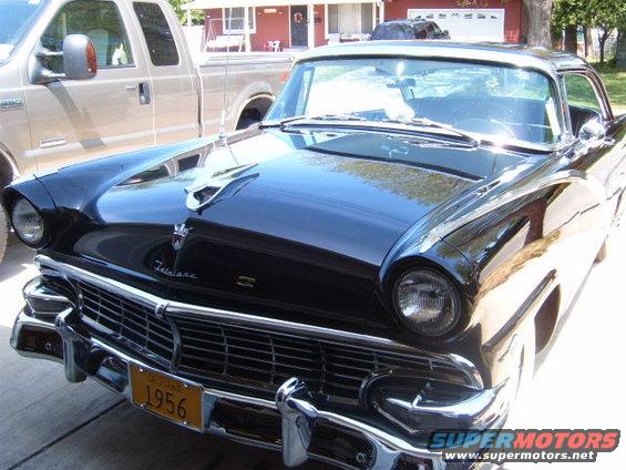Black 1956 Ford Fairlane parked in front of a house with a pickup truck next to it