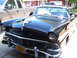 1956 Ford Fairlane - A shiny black 1956 Ford Fairlane is parked in a driveway, with a modern pickup truck beside it.