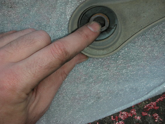 Hand pointing to a worn control arm bushing with a hex bolt head visible