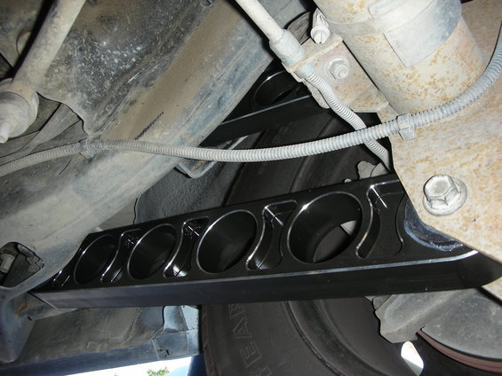 Black aftermarket rear control arm with circular cutouts, viewed from underneath