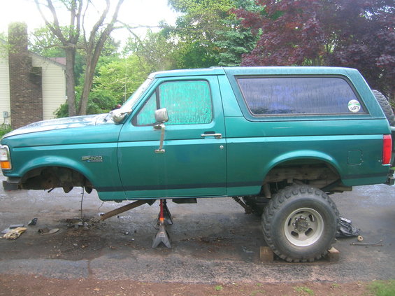 Green 1996 Ford Bronco on jack stands with front wheels removed, parked on asphalt