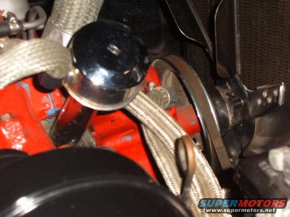 Close-up of engine parts including a chrome cap, red block, and fan belt