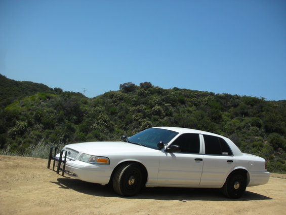 White 2004 Ford Crown Victoria police car with push bumper parked on dirt road