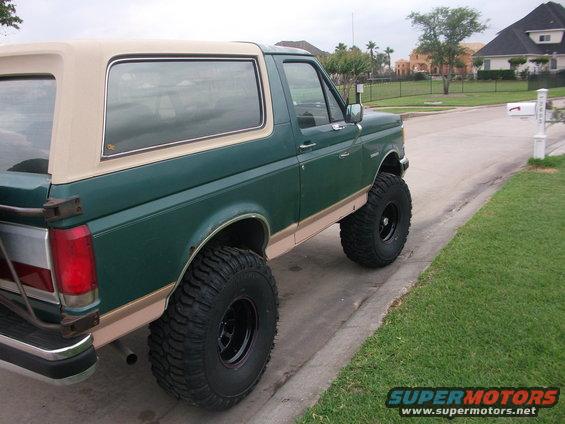 1989 Ford Bronco, green with tan top, lifted with large tires, parked on street