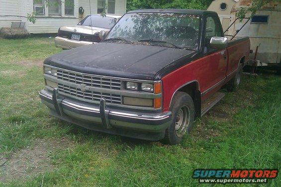 Front view of a red and black pickup truck, with a sedan in the background