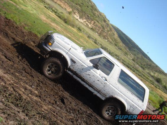 White 1992 Ford Bronco covered in mud driving up a steep, grassy hill