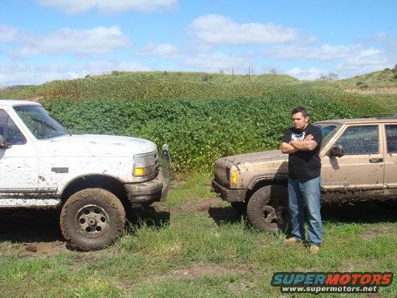 White 1992 Ford Bronco front driver side, covered in mud, parked next to a tan Jeep Cherokee and a man