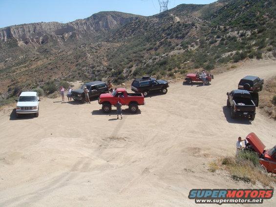 group of off-road vehicles parked on a dirt road in a hilly, arid area