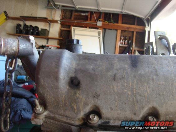 Close-up of a dirty engine valve cover with a chain hanging nearby. Garage interior in background