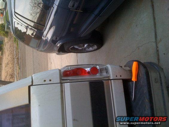 White truck's rear light assembly and dark SUV's side panel and wheel