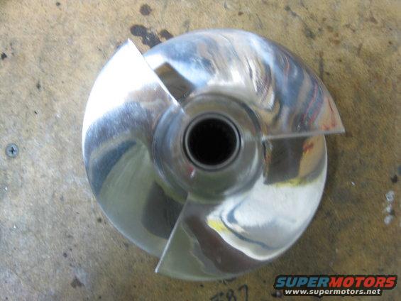 Polished metal jet ski impeller with three blades, resting on a wooden surface