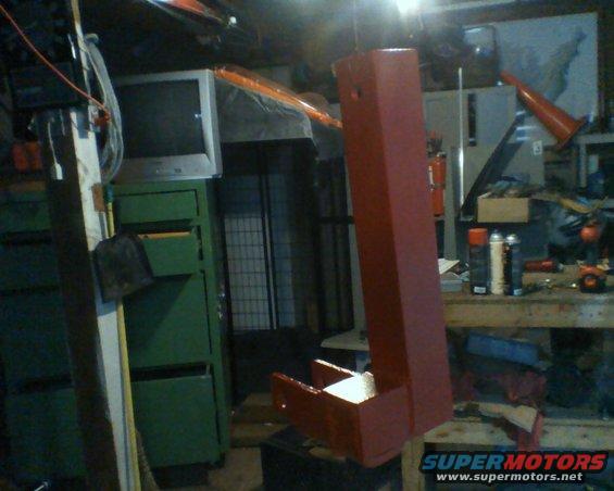 Red metal part with a box-like end, hanging in a cluttered garage