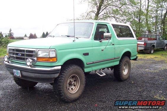Green 1992 Ford Bronco with aftermarket wheels and tires, parked on gravel
