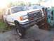 1989 Ford Bronco - White Ford Bronco with a rusty bull bar, lifted front end supported by a forklift.