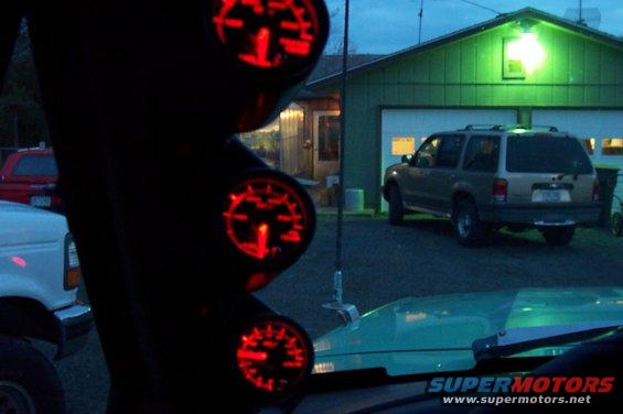 Interior view of red-lit gauges with a tan SUV parked in front of a garage