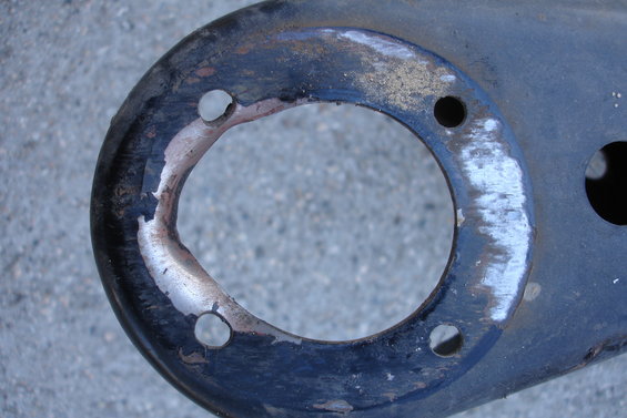 Close-up of a dark, circular metal part with chipped paint and four bolt holes