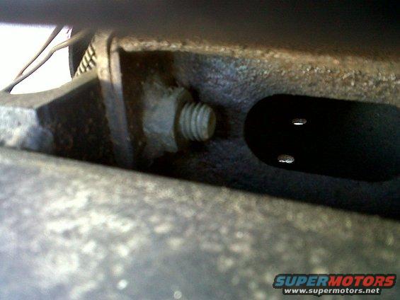 Close-up of a bolt threaded into a metal engine component with two small holes visible