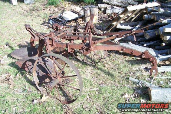 Rusted farm plow with a large spoked wheel in a grassy area