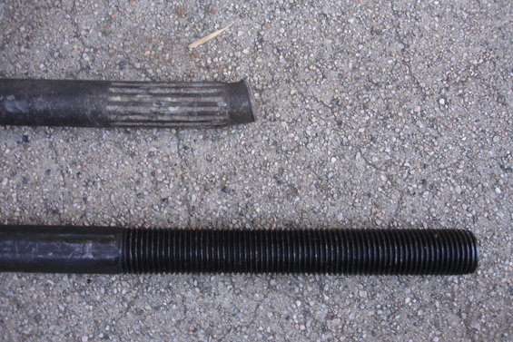 Two metal rods, one with splines and a cut end, the other threaded, lie on a concrete surface