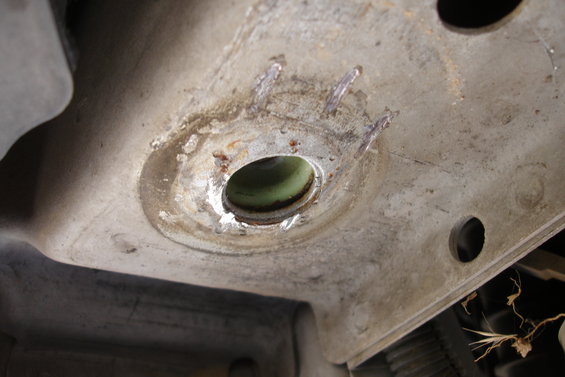 Close-up of a corroded metal subframe part with a green bushing and weld marks
