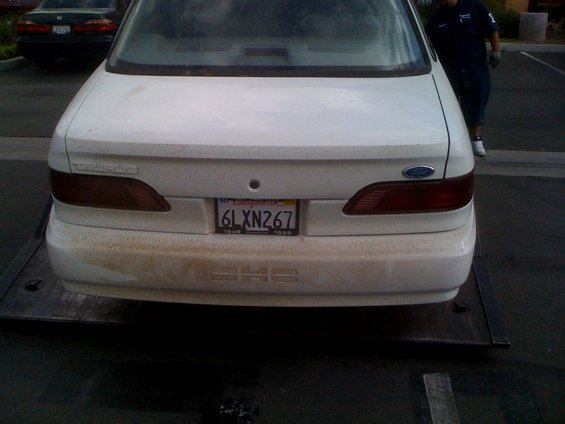 White 1992 Ford Taurus sedan rear view, dirty, on a flatbed truck