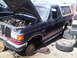 1986 Ford Bronco - Junkyard Bronco missing wheels and parts, hood is open showing the engine bay.