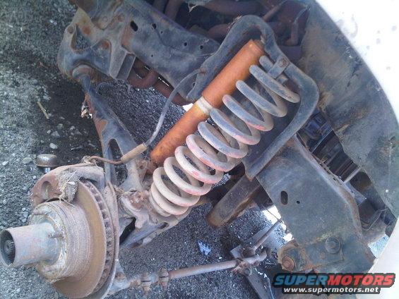 Rusty front suspension with coil spring and shock absorber, disc brake rotor visible