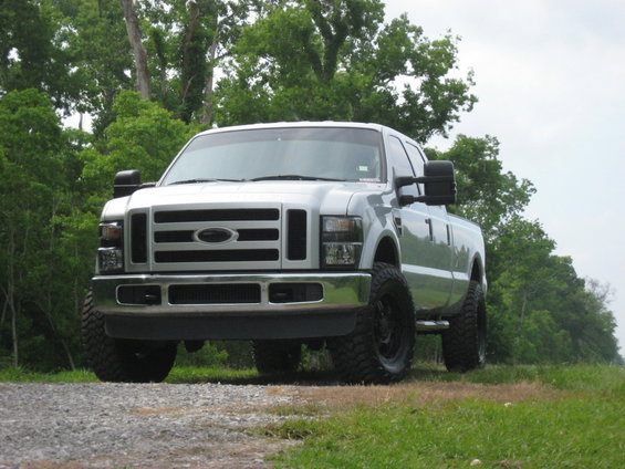 Silver Ford F-250 pickup truck parked on a gravel road with trees in the background
