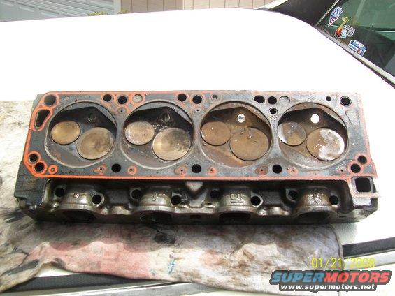 Engine cylinder head with valves visible, resting on a white surface