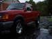 1997 Ford Ranger - Red 1997 Ford Ranger pickup truck parked on wet asphalt driveway with trees in background.