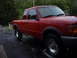 1997 Ford Ranger - Red 1997 Ford Ranger extended cab pickup truck parked on wet asphalt with trees in background.