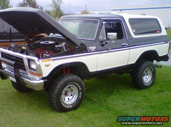 Two-tone black and white Ford Bronco with hood open, showing engine. Lifted suspension and off-road tires
