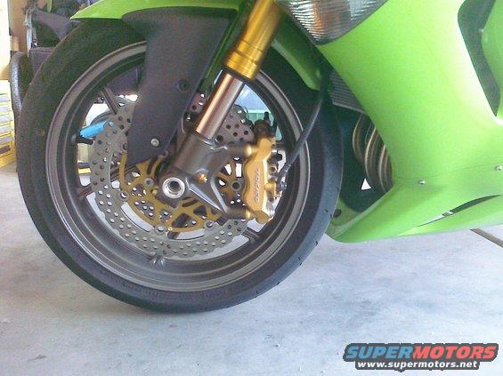 Green motorcycle front wheel with gold brake caliper and dual discs, silver rim, and part of green fairing