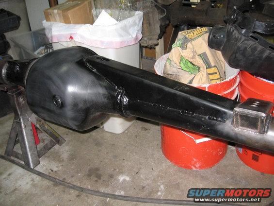 Black painted rear axle housing on jack stands, with red buckets and a bag of material in the background