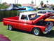 1992 Ford Bronco - A classic red and white pickup truck is displayed with its hood open at a car show, revealing the engine.