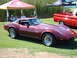 1992 Ford Bronco - A maroon Chevrolet Corvette is displayed at an outdoor car show next to a red pickup truck.
