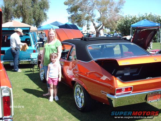 Woman and girl by an orange classic car. Another vehicle and person in background