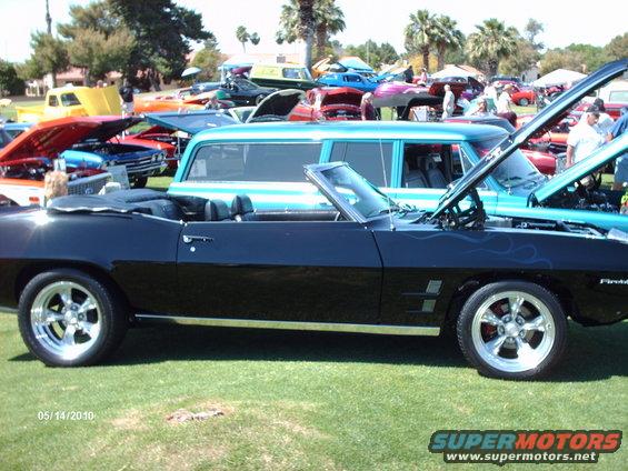 Black convertible with blue flames and chrome wheels parked on grass at a car show